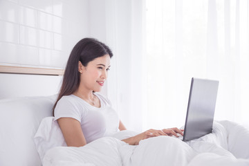 Beautiful asian woman sitting on bed and using laptop computer