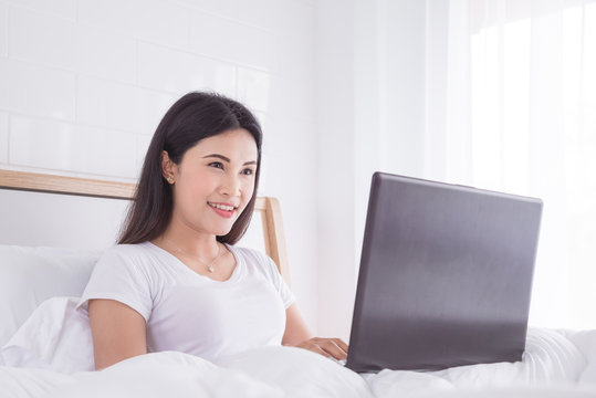 Beautiful asian woman sitting on bed and using laptop computer