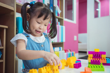 Little asian preschool age girl playing plastic blocks at nursery