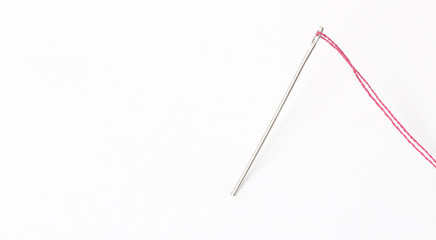 Sewing needle with red thread through the white background