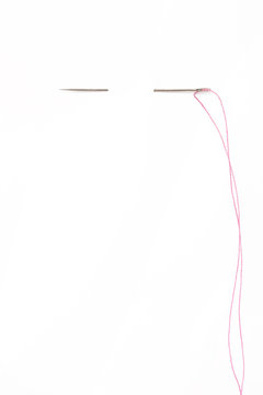 Sewing needle with red thread through the white background