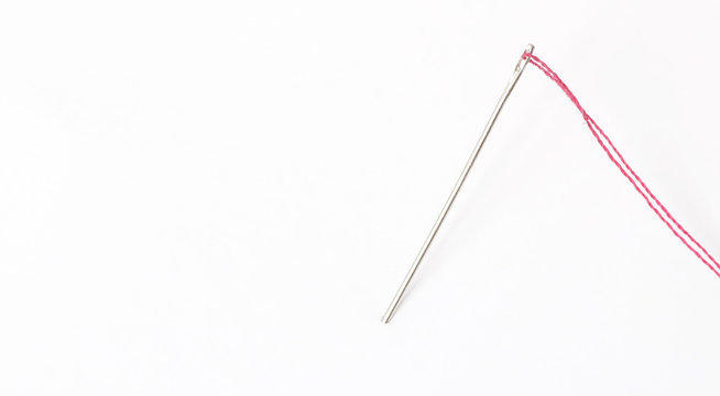 Sewing needle with red thread through the white background