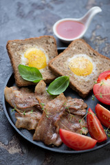 Breakfast with fried bacon, eggs in the basket and tomatoes, selective focus, close-up