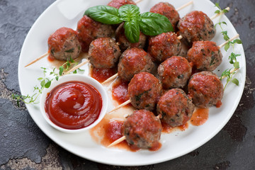 Skewers with baked meatballs in tomato sauce served on a white plate, horizontal shot