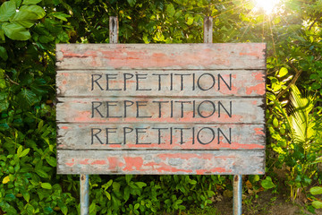 Repetition, Repetition, Repetition motivational quote written on old vintage board sign in the forrest, with sun rays in background.