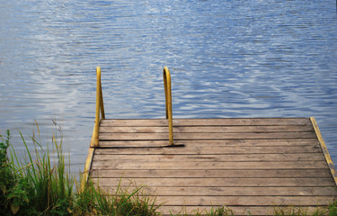 Wooden pier on the shore of a lake with a yellow staircase in the water