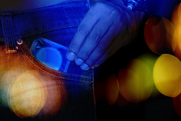 Man holding condom in the blue jeans with bokeh.