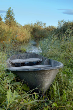 A wooden boat lies on the grassy bank of the river