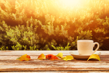 Naklejka na ściany i meble coffee cup over wooden table and autumn leaves in front of autumnal background