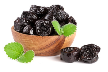 Dried plums or prunes with a mint leaf in wooden bowl isolated on white background
