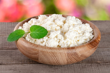 Cottage cheese in a wooden bowl on board with blurred garden background