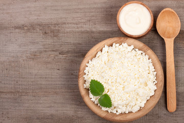 Cottage cheese in a wooden bowl with sour cream on old wooden background with copy space for your text. Top view