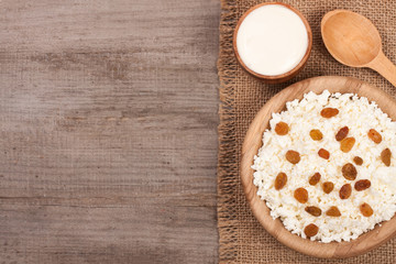 Cottage cheese in bowl with sour cream and raisins on old wooden background with copy space for your text. Top view