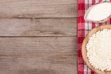 Cottage cheese in a wooden bowl with sour cream on old wooden background with copy space for your text. Top view