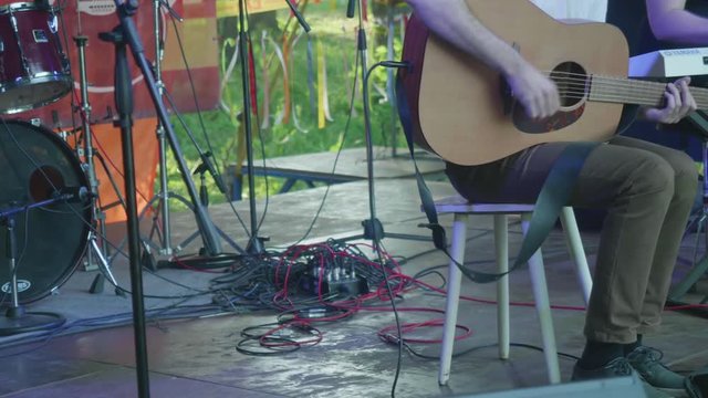 Man performs on stage playing guitar and sitting on chair.