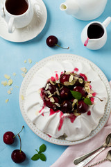 Homemade meringue cake Pavlova with whipped cream, fresh cherry and  sauce  on light concrete texture background.Selective focus. Top view, space
