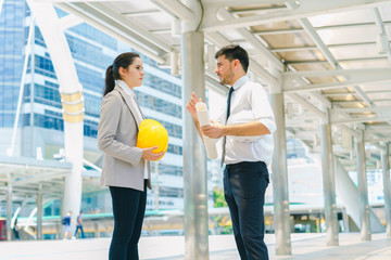 Engineer holding safety helmet and holding drawing discuss in building project planning, working together, concept of business negotiation and deal benefit.