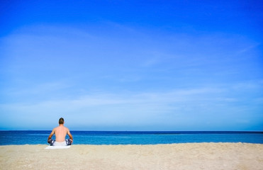 Fototapeta na wymiar A man doing meditation or yoga on the beach on sunshine day