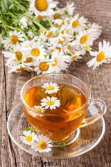 Herbal tea with fresh chamomile flowers on old wooden background