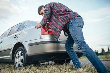 Man pushing broken car, side view