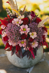 Red autumn bouquet of roses, chrysanthemums and feathers in a vase from pumpkin