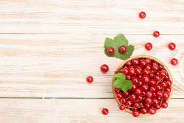 Red currant berries in a wooden bowl with leaf on the light wooden background with copy space for your text. Top view