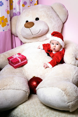 Cute little christmas child In the arms of a teddy bear wearing santa claus suit, with a funny look. Christmas card