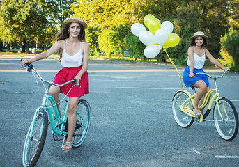 Two stylish young female friends on a bicycle in park. Best friends enjoying a day on bike