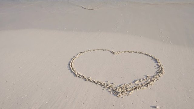 Handwriting shape of heart drawn on sand at maldivian beach, travel destinations concept
