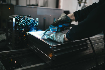 Metallurgy industry. Factory for production of heavy pellet stoves and boilers. Close up of manual worker welder on his job. Extremely dark conditions and visible noise.