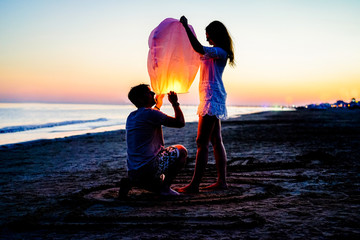 Couple of lovers lighting sky lantern on the beach at sunset - Young people celebrating their relation anniversary in summer vacation - Love and travel concept - Main focus on man head - Retro filter © DisobeyArt