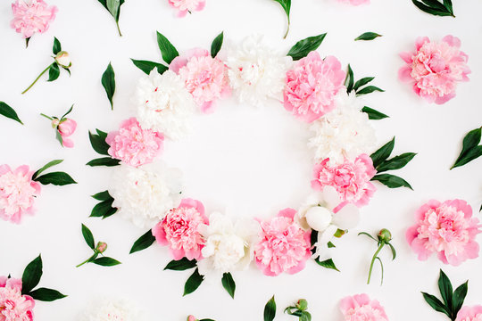 Frame of pink peony flowers, branches, leaves and petals with space for text on white background. Flat lay, top view. Peony flower texture.