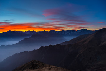 Fototapeta na wymiar Colorful sunlight behind majestic mountain peaks of the Italian - French Alps, viewed from distant. Fog and mist covering the valleys below, autumnal landscape, cold feeling.