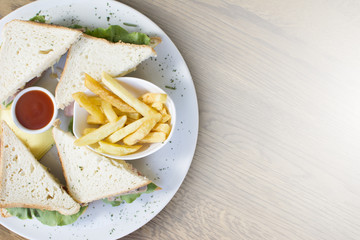 Club sandwich with chicken breast, bacon, tomato, cucumber, and herbs. French fries on the side.
