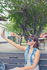 Beautiful young sexy woman using smartphone sitting on a bench in the park. Bali island, Indonesia.