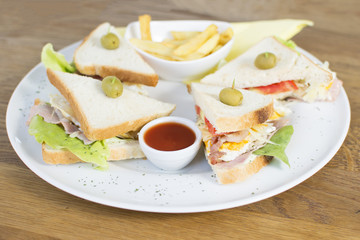 Club sandwich with chicken breast, bacon, tomato, cucumber, and herbs. French fries on the side.