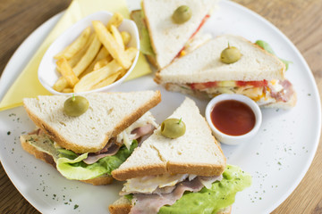 Club sandwich with chicken breast, bacon, tomato, cucumber, and herbs. French fries on the side.