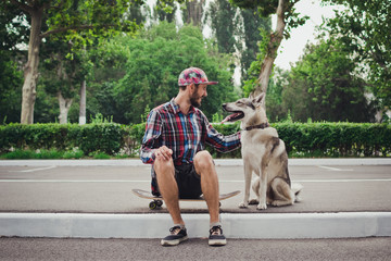 Obraz premium Young hipster man sitting on skateboard with siberian husky dog on street road