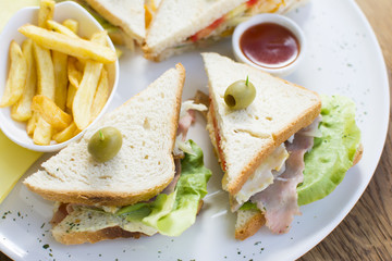 Club sandwich with chicken breast, bacon, tomato, cucumber, and herbs. French fries on the side.