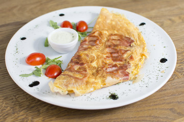 Scrambled eggs with ham on a plate on the wooden table. Tomato and sour cream on the side.