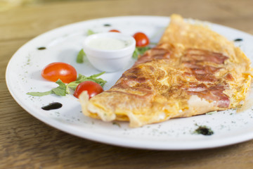 Scrambled eggs with ham on a plate on the wooden table. Tomato and sour cream on the side.