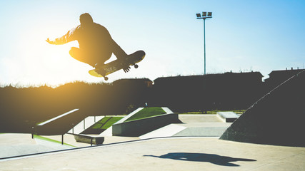 Silhouette of skater jumping on ramp at city park - Young man performing tricks and skills with skateboard at sunset  - Youth,extreme sport concept - Focus on body - Vintage retro filter © DisobeyArt