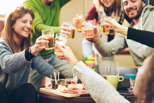 Group of happy friends cheering with beer after skiing day in bar pub restaurant - Young people toasting appetizer in brewery chalet - Concept about good and positive mood - Focus on right bottom hand