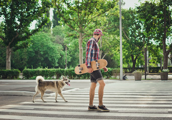 Young hipster man walking with skateboard and siberian husky dog on street road