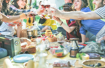 Happy friends cheering with wine glasses at pic-nic lunch outdoor - Young students having fun doing a toast and eating on nature - Food and youth concept - Focus on center glasses - Vintage filter