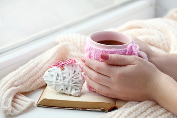 Woman hands holding cup of coffee near the window