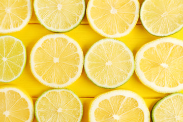 Slices of limes and lemons on yellow wooden table