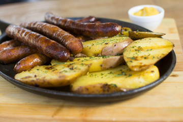 Grilled sausages and potatoes on wooden cutting board. Mustard on the side.