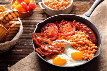 English Breakfast with sausages, grilled tomatoes, egg, bacon, beans and bread on frying pan.