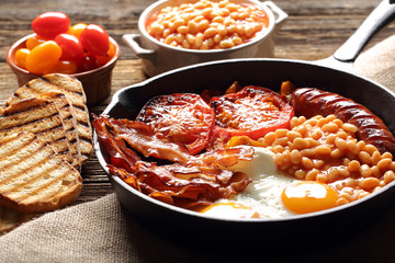 English Breakfast with sausages, grilled tomatoes, egg, bacon, beans and bread on frying pan.